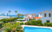 Luxurious Mediterranean seaside resort with pool, villas, palm trees, and stunning sea view.