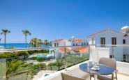 Scenic coastal balcony view overlooking Mediterranean-style Paphos Villa, palm trees, and tranquil sea.