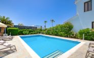 Paphos Villa with Tranquil outdoor pool area with loungers, umbrellas, and lush greenery under clear blue skies.