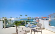 Serene coastal balcony overlooking Mediterranean buildings, palm trees, and ocean on a sunny day.