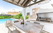 Villa in Paphos outdoor living space with stone table, grill, pool, and lounge chairs under umbrellas.