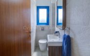 Kissonerga Villa Modern and minimalist bathroom with light stone tiles, sleek white vanity, and blue accents.