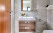 Modern bathroom interior Kissonerga Villa with sleek wooden vanity, mirror, and accessories in contemporary design.