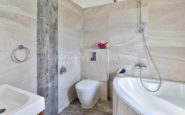 Kissonerga Villa with Modern and elegant bathroom with grey and beige tones, featuring a sleek toilet and bathtub.