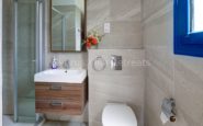 Kissonerga Villa with Modern bathroom with glass shower, wood vanity, wall-mounted toilet, and blue window.