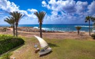 Kissonerga Villa Tranquil coastal scene with boat, palm trees, ocean, and sky on a sunny day.