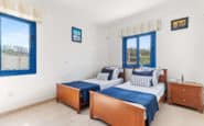 Holiday villas in Paphos with Cozy bedroom with two beds, wooden frames, blue accents, and natural light.