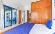 Modern, serene bedroom with blue accents, wooden wardrobe, and ample natural light.