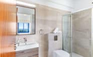 Modern bathroom with neutral tones, glass shower, floating vanity, and natural light.