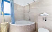 Modern, elegant bathroom with corner bathtub, minimalist toilet, natural light, and neutral colours.