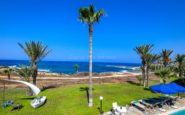 Seaside palm tree scene with pool area, boat, and hammock at holiday villas in Paphos