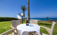 A romantic outdoor dining setting by the sea with wine, chairs, and stunning coastal views.