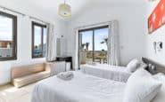 Modern villa for rent, minimalist bedroom with white beds, vibrant artwork, and scenic balcony view.