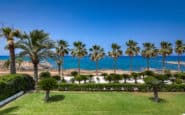 Seaside villa hire Cyprus retreat with palm trees, beach, and ocean under clear blue sky.