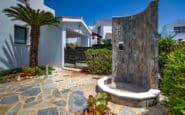 Villa Hire Cyprus with Luxurious outdoor shower in landscaped garden with modern building and lush greenery.