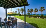 Villas for rent with Luxurious coastal patio with dining setup, lush lawn, palm trees, and ocean view.