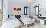 Modern, minimalist bedroom with two beds, colorful painting, and natural light flooding the room.