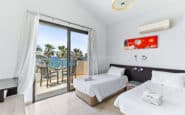 Paphos holiday with ocean view balcony, two beds, red painting, and minimalist decor.