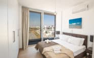 Modern minimalist bedroom with city view balcony, white linens, and sleek furniture in holiday rentals in Cyprus Protaras