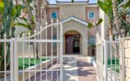 Luxurious Mediterranean villa in Kato Paphos entrance with stone archway, lush greenery, and wrought iron gate.