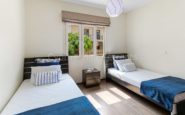 Modern twin bedroom with white and blue bedding, dark brown accents, and natural light.