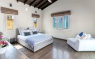 Well-furnished bedroom with cozy bed, bright windows, and stylish decor creating serene ambiance.