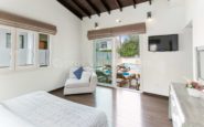 Bright and modern bedroom with natural light, wooden ceilings, cozy armchair, and patio view.