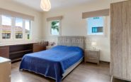 Contemporary bedroom with blue bedspread, wooden furniture, natural light, and floral decor.