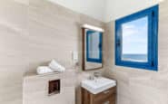 Modern Holiday Villas in Cyprus with minimalist bathroom with sleek design, cream tiles, blue window frame, and ocean view.