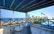 Holidays Villas in Cyprus with Luxurious ocean view terrace with wicker furniture, blue canopy, and lush garden.