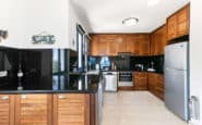 Modern kitchen in Holiday Villa in Paphos with black glossy countertops, wooden cabinets, stainless-steel appliances, and sleek design.