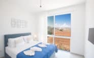 Cyprus Villa Rentals with Cozy minimalist bedroom with blue accents, white bedding, and expansive outdoor view.