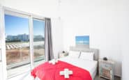 Modern and airy bedroom with red accents, rustic nightstand, and panoramic view of Protaras strip.