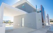 Modern two-story house with minimalist design, carport, and sleek aesthetic in residential area.