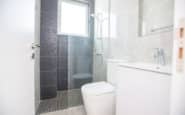 Modern, minimalist bathroom with white and gray tones, featuring a sleek shower and vanity.