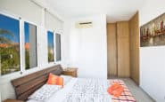 Modern bedroom with minimalist design, white bedding, wooden wardrobe, and vibrant accents.