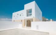 Modern minimalist house with clean lines, white facade, and geometric design under clear blue sky.