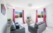 Modern white living room with black leather sofas, vibrant magenta curtains, and contemporary artwork ideal for Villa hire Cyprus.