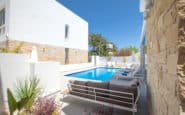 Modern outdoor swimming pool area with lounge chairs, sofa, and lush landscaping for relaxation in Cyprus Protaras Villa Rentals.