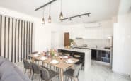 Modern, sleek kitchen and dining area with white marble flooring, black accents, and industrial lighting in Cyprus Protaras Villa Rentals.