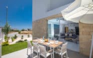 Modern outdoor dining area with white chairs, open umbrella, and sleek design in Cyprus Protaras Villa Rentals..