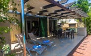 Stylish outdoor patio with pergola, sunbeds, dining area, and barbecue grill.