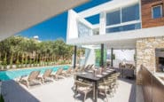 Luxurious modern Ayia Napa Villa with pool, dining area, sun loungers, and lush landscaping under clear blue sky.