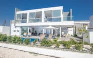 Modern luxury villa with sleek design, floor-to-ceiling windows, outdoor living area, and swimming pool in Protaras.