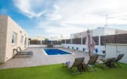 Modern outdoor pool area with lounge chairs, greenery, and sleek fence for villa hire in Cyprus.