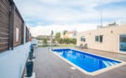 Modern pool area with wooden deck, lounge chairs, and potted plants in a serene setting.