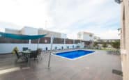 Modern outdoor pool area with dining, lounge chairs, shade sail, and tiled deck.