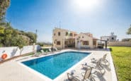 Villa Rentals in Protaras offeriing luxurious poolside oasis with sunbeds, blue water, green lawn, and beige villa in sunny countryside.