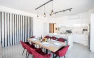 Modern, minimalist dining and kitchen area with red chairs, industrial lighting, and sleek design a good choice of Protaras Holiday Rentals.