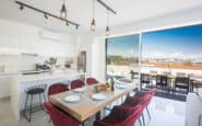 Protaras Holiday Rentals presenting modern open-concept kitchen and dining area with sleek white cabinetry and urban skyline view.